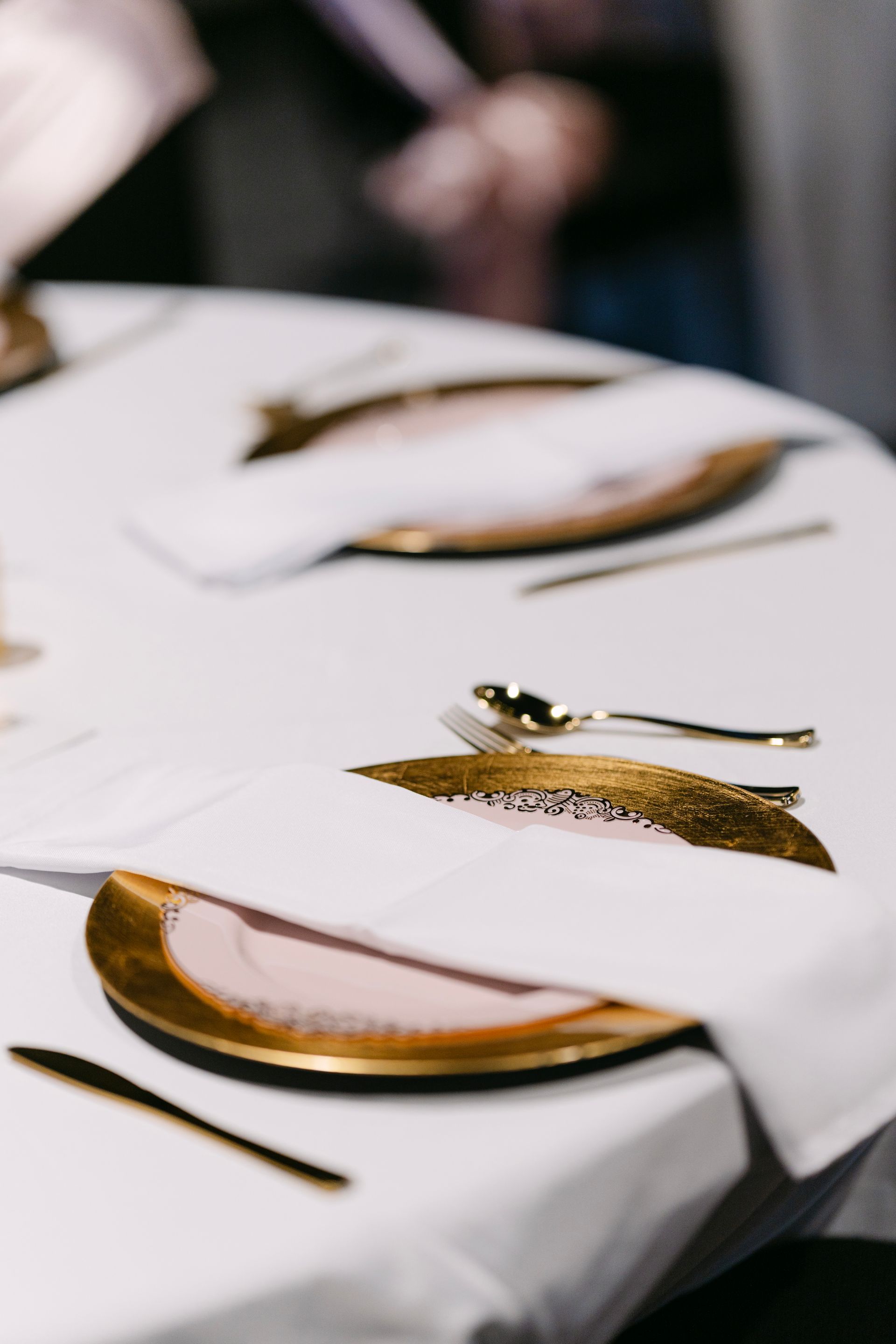 Table setting with gold-rimmed plates, silverware, and folded white napkins on a white tablecloth.