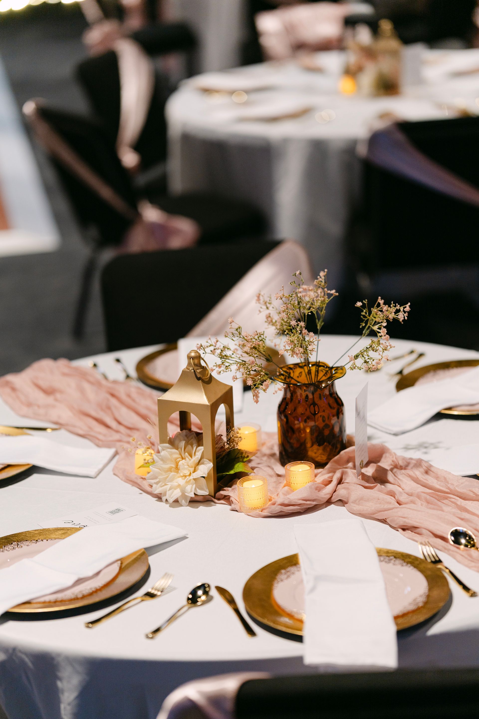 Wedding reception table setting with gold accents and blush-colored runner.