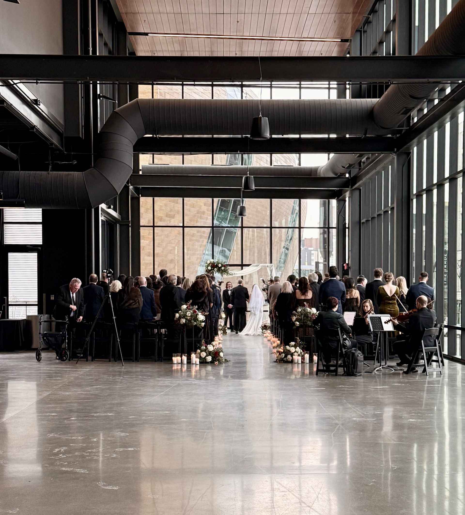 Wedding ceremony inside a modern building with large windows. Guests seated, couple at the altar.
With Love, Wedding management, Milwaukee Wedding Coordinator