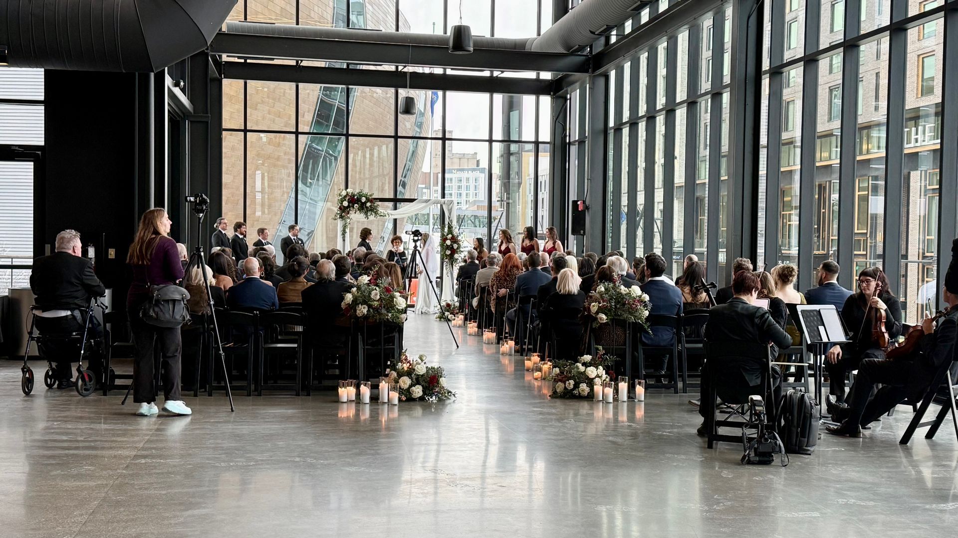 Wedding ceremony in modern venue with floor-to-ceiling windows. Guests seated, couple at altar.
With Love, Wedding management, Milwaukee Wedding Coordinator
