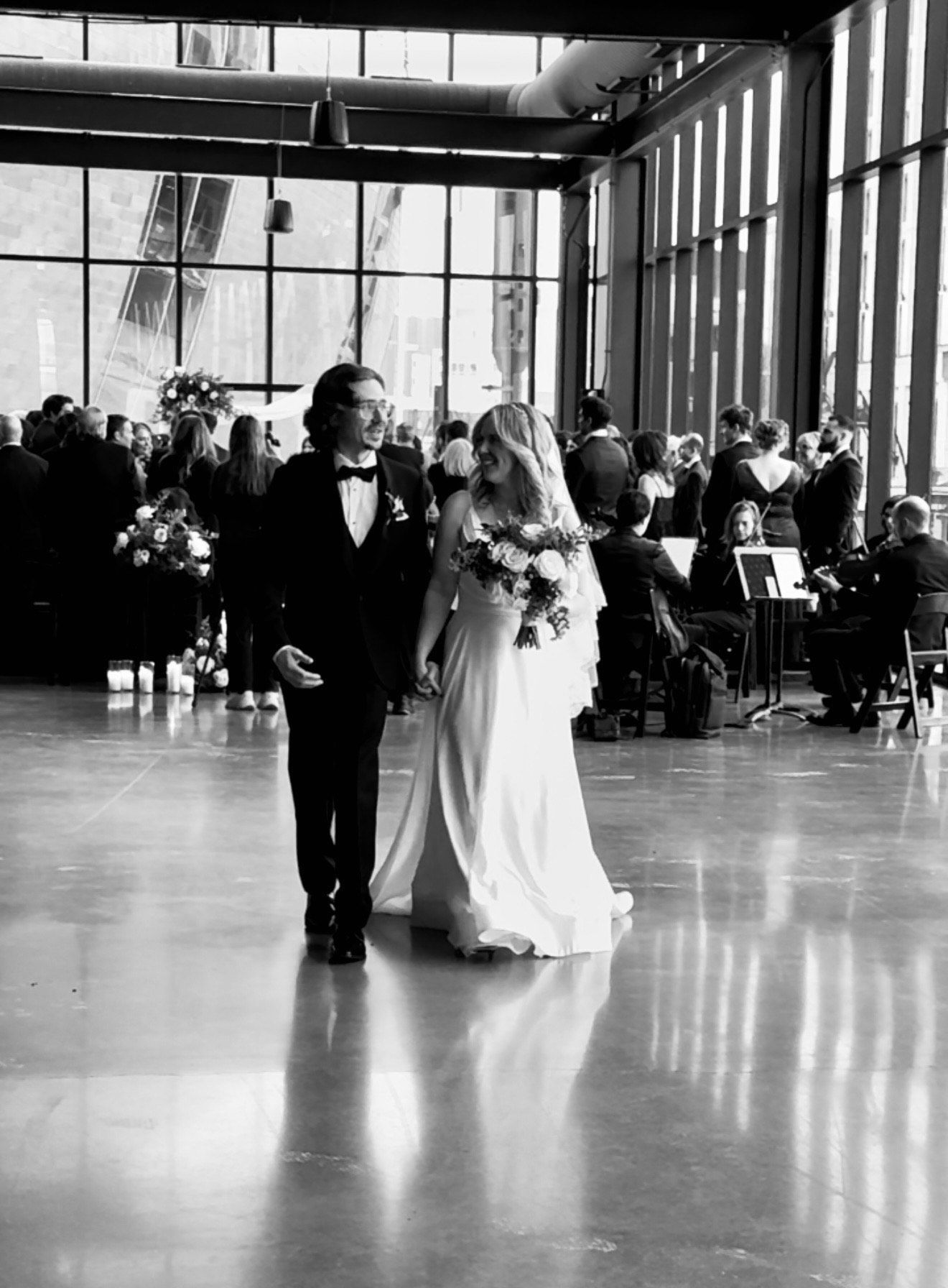 Newlyweds walk hand-in-hand down the aisle. The bride wears a white gown, and the groom a suit. Indoor wedding.
With Love, Wedding management, Milwaukee Wedding Coordinator
