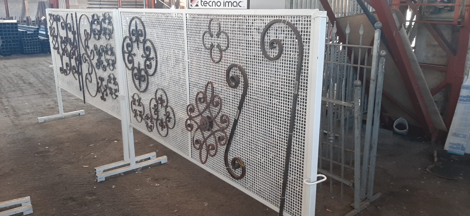 Una recinzione metallica con un motivo è posta in cima a un campo sterrato.