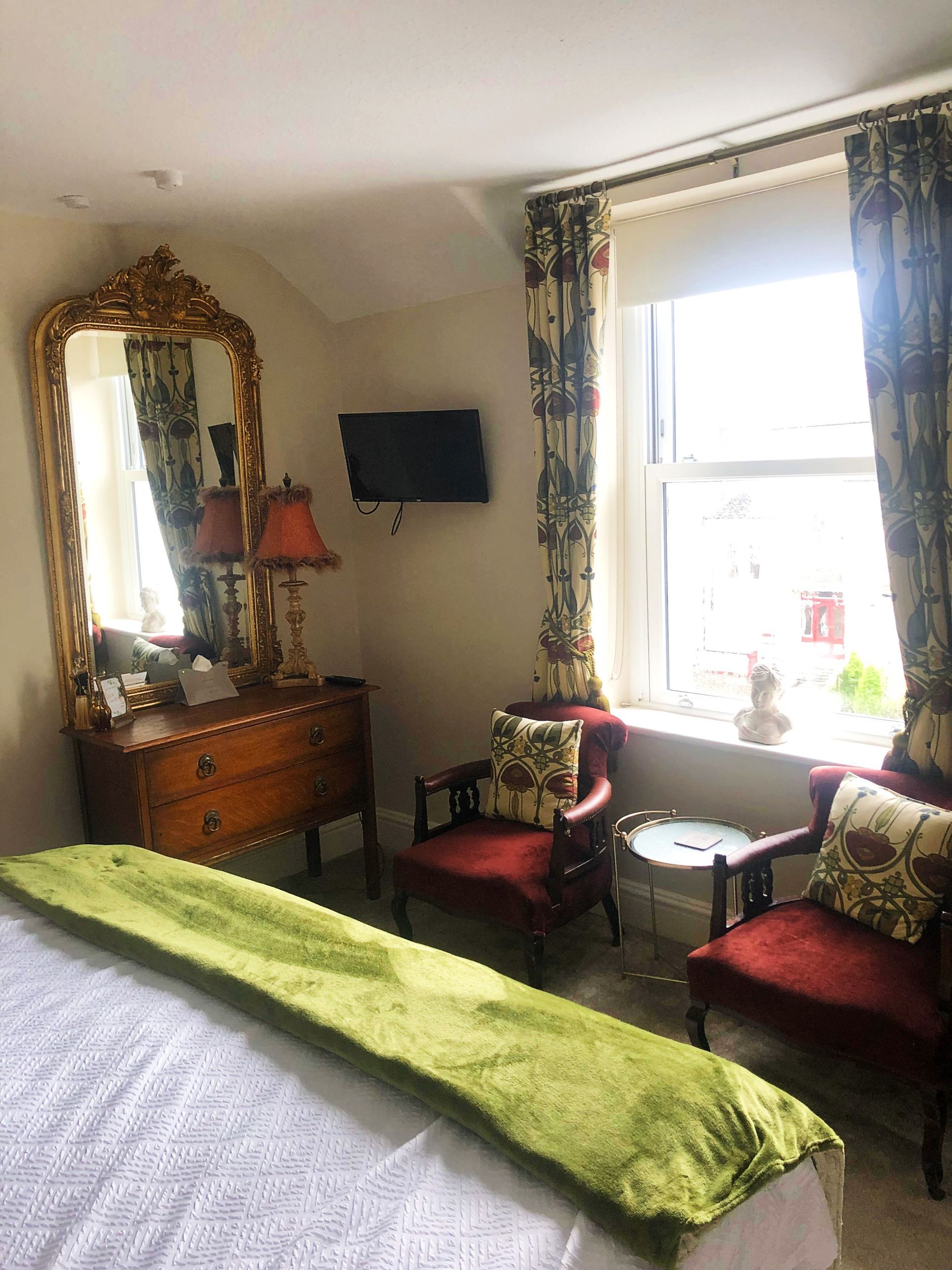 A bedroom with a bed , chairs , dresser , mirror and television.