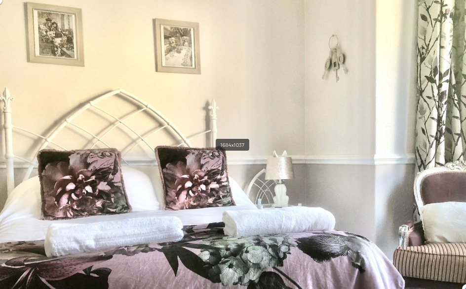 A bedroom with a bed , chair , lamps and pictures on the wall.