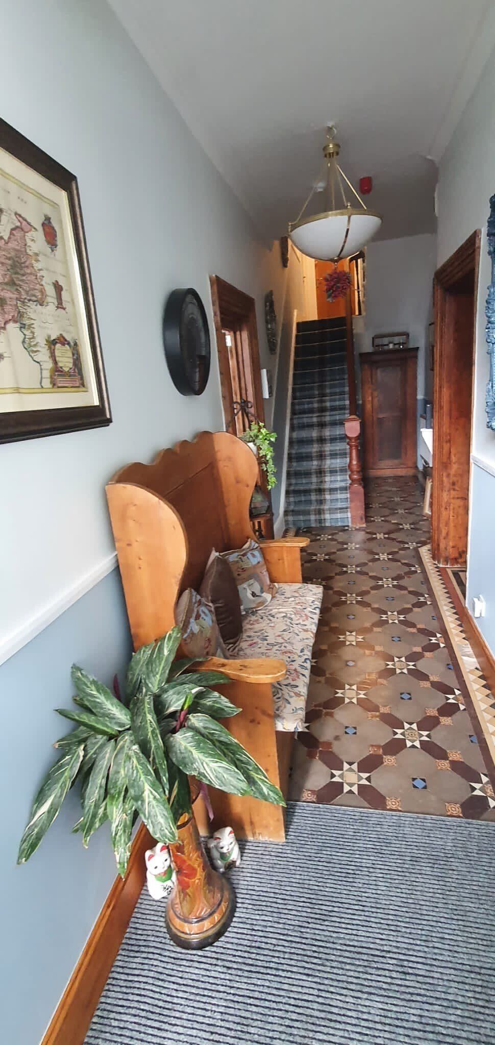A long hallway with a bench , chair , plant and stairs.