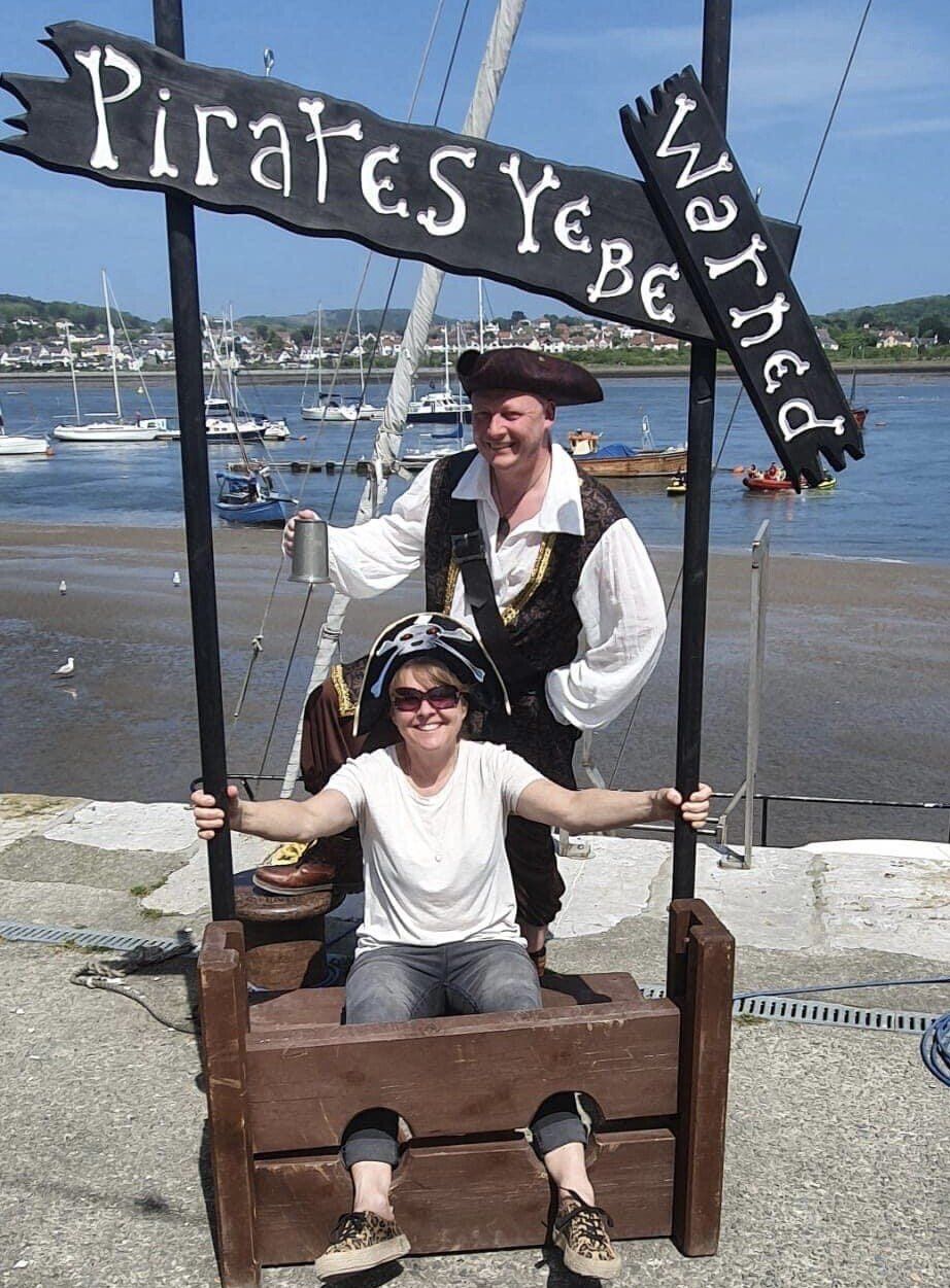 A woman is sitting in a wooden stockade under a sign that says pirates yebe
