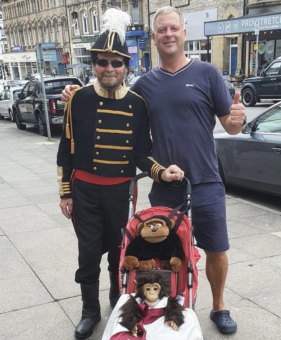 Two men posing with a stuffed monkey in a stroller