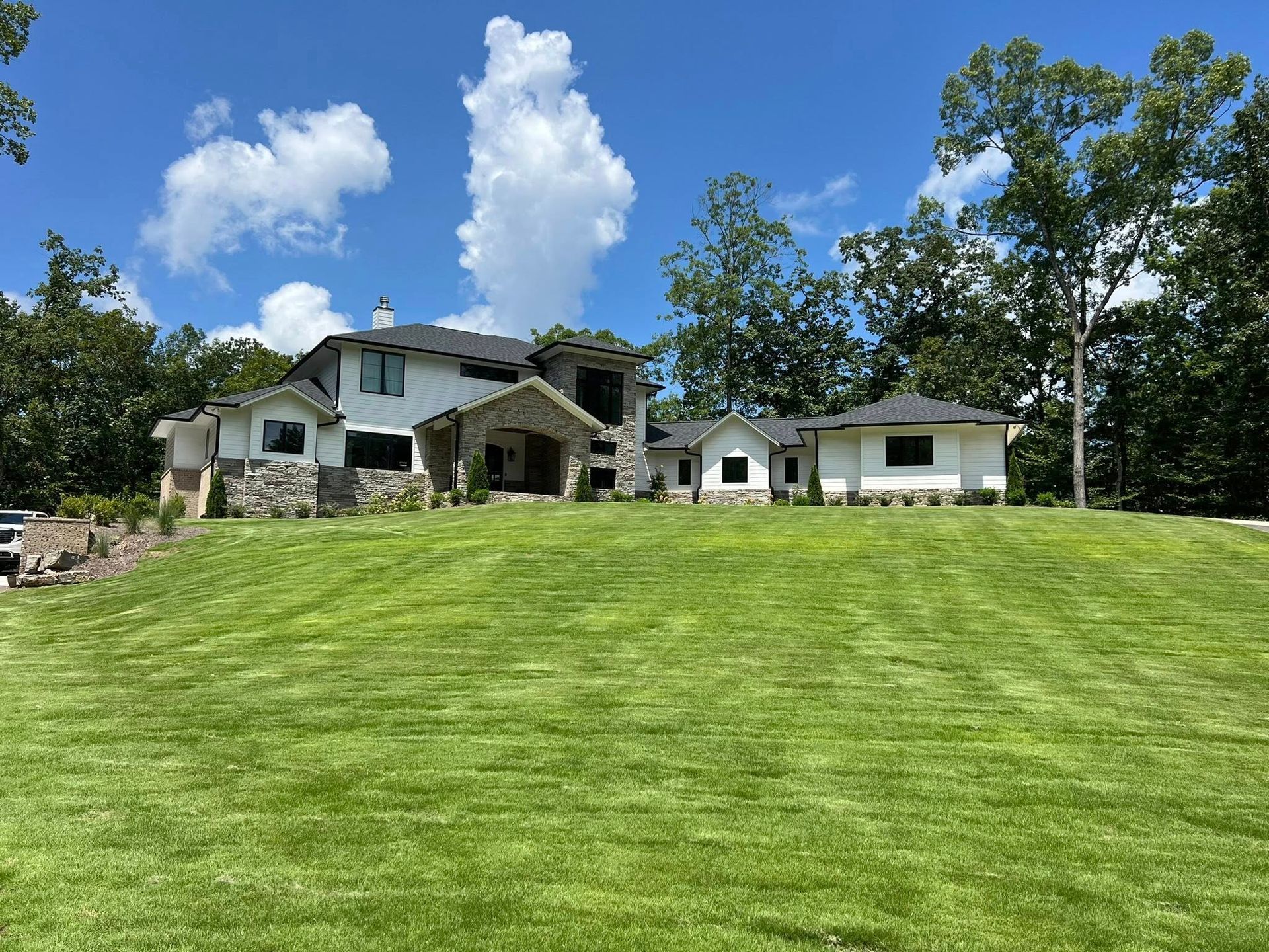 A large house is sitting on top of a lush green hill surrounded by trees.