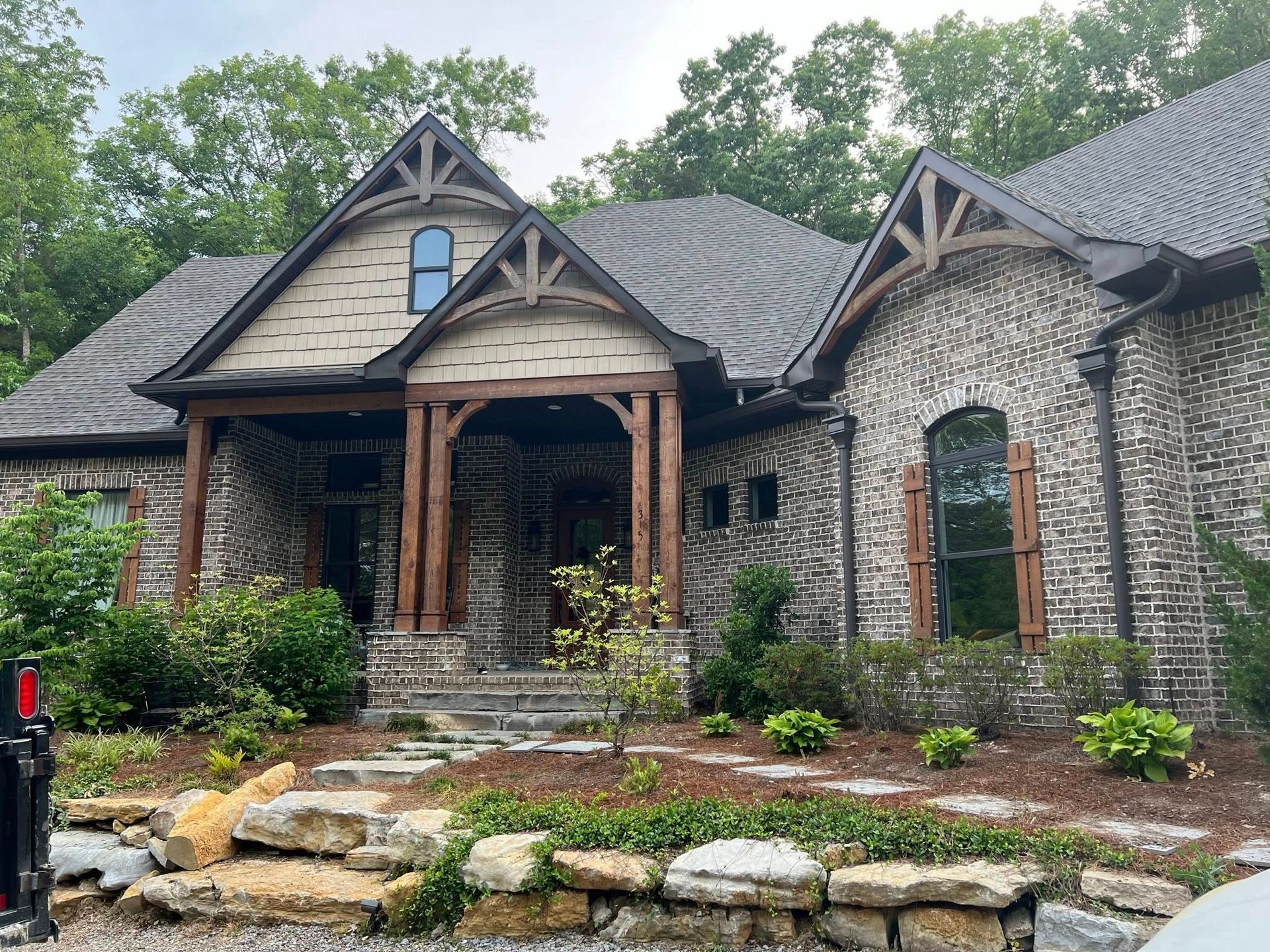A large brick house with a gray roof is surrounded by trees.
