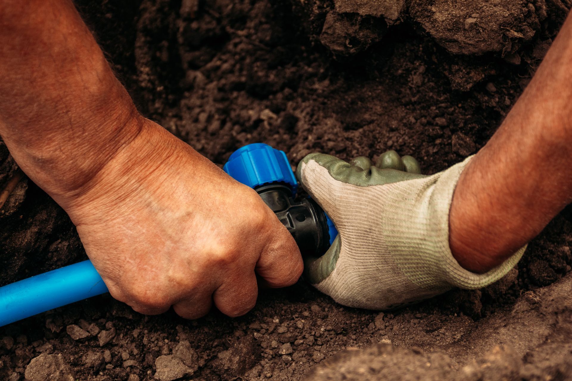A person is working on a pipe in the dirt.