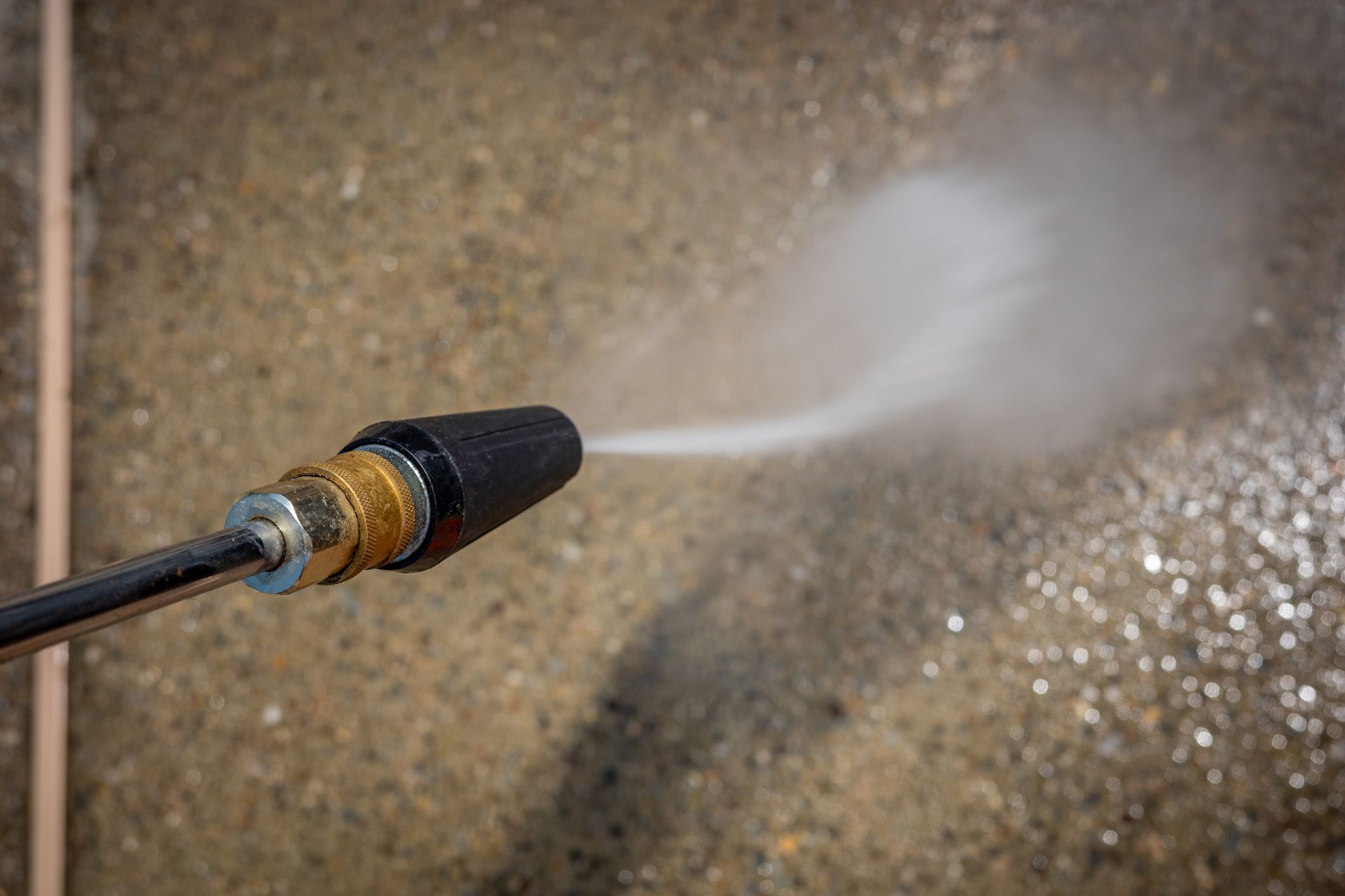 Pressure washer spraying water onto a concrete surface, creating a mist.