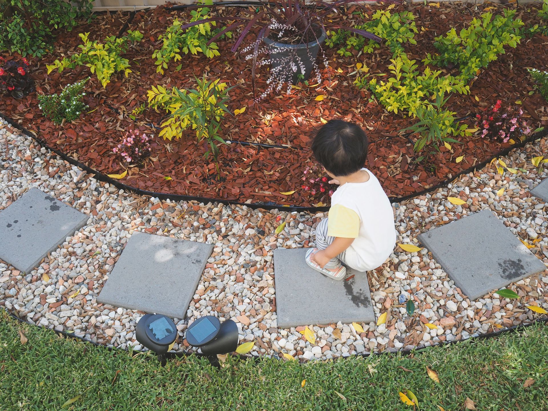 Child kneeling on stepping stones next to a landscaped garden bed filled with mulch and plants.