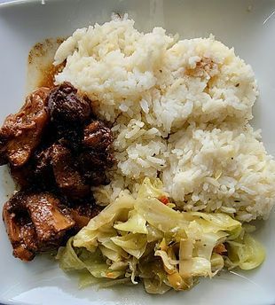 A white plate topped with rice , meat and cabbage.