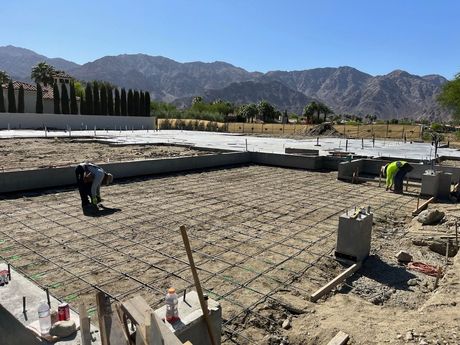 A group of construction workers are working on a concrete foundation with mountains in the background.