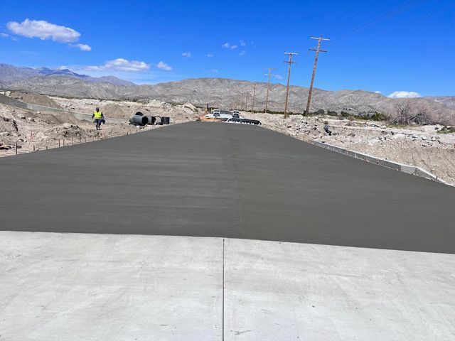 A concrete road is being built in the desert with mountains in the background.