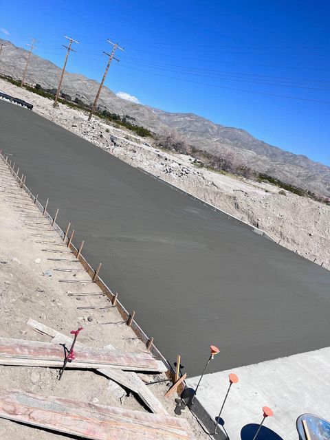 A concrete road is being built in the desert with mountains in the background.