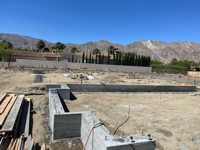A construction site with a house in the background and mountains in the background