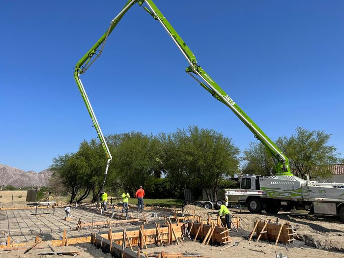 A green concrete pump is being used on a construction site