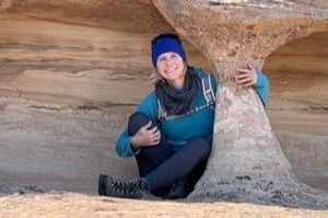 A woman is sitting next to a large rock formation.