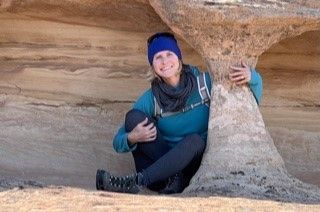 A woman is sitting next to a large rock formation.