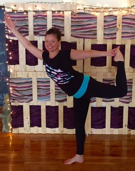 A woman is doing a yoga pose in front of a wooden wall