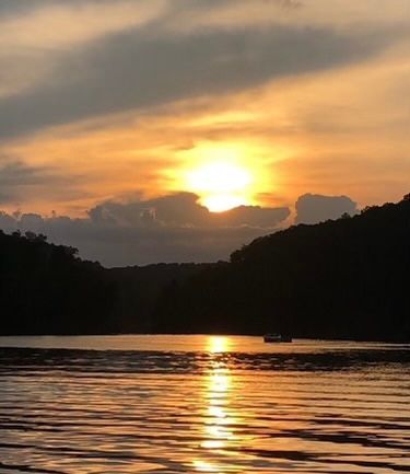 Sunset over water with hills on either side; golden light reflects on the water's surface.