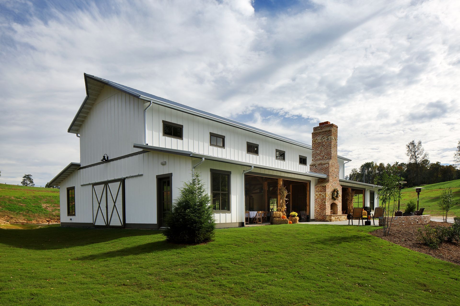White barn with a gray roof and stone chimney on a grassy hill under a partly cloudy sky.