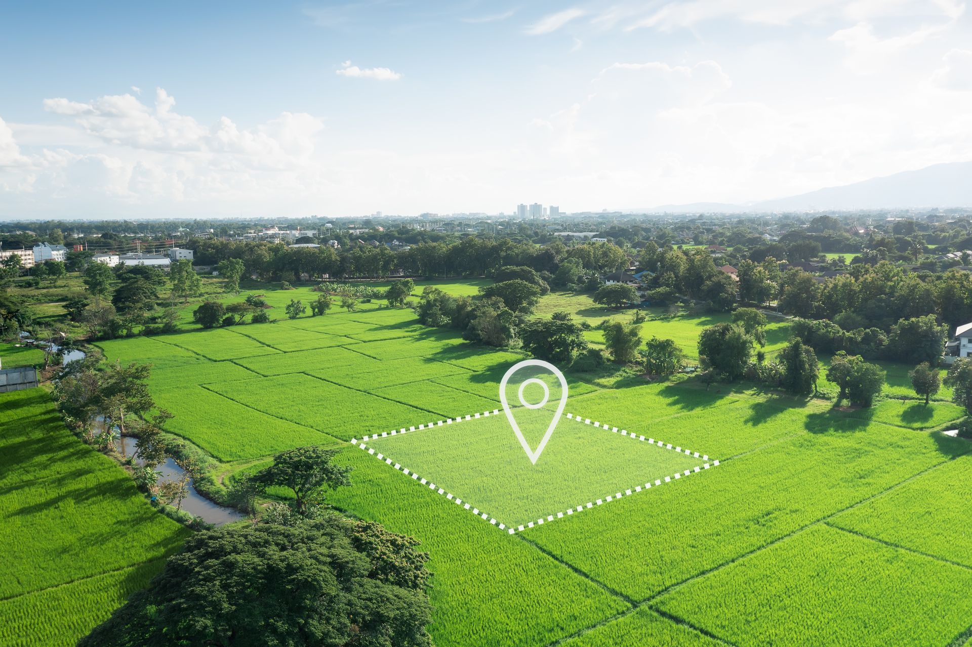 Aerial view of green field with location marker; town in background.