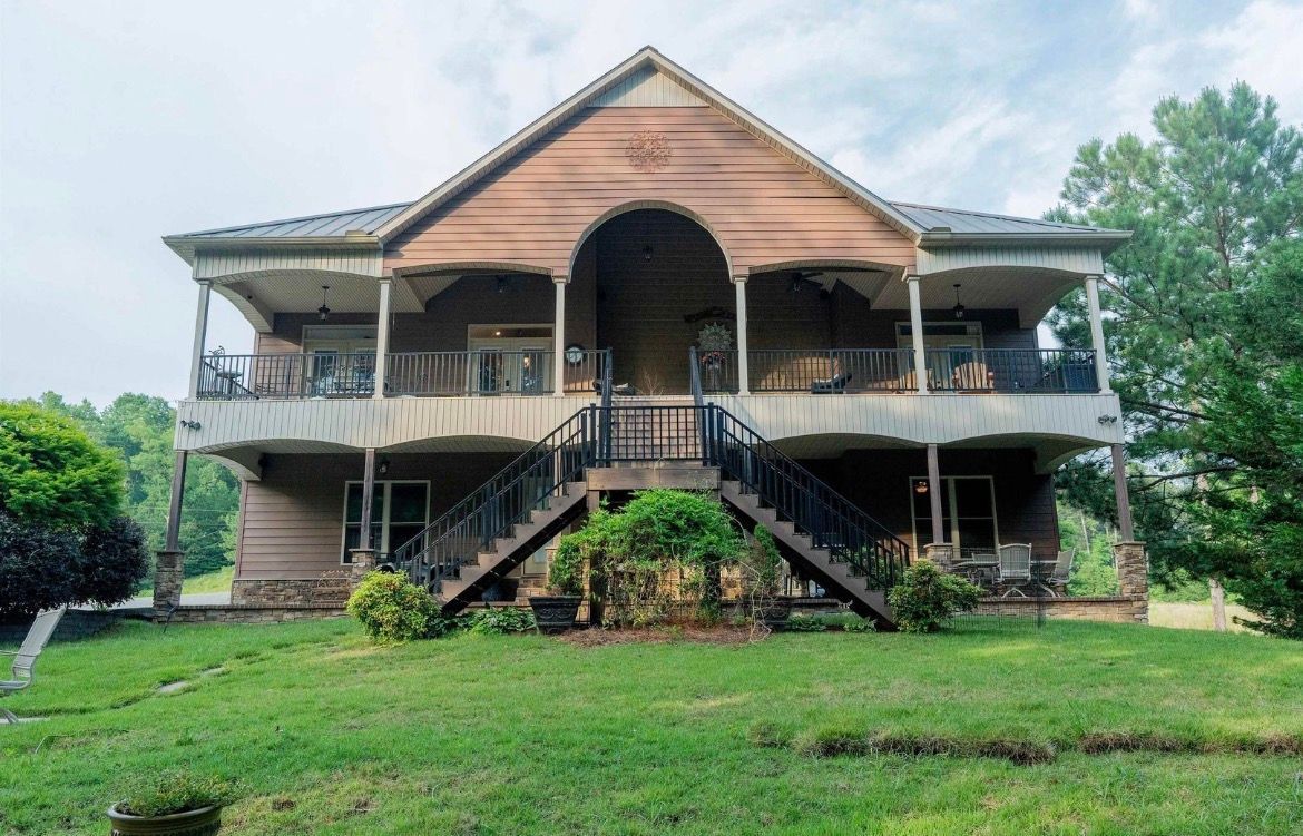Two-story green house with a shingled roof, a manicured lawn, and mountain backdrop.