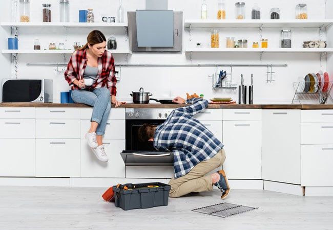 Young Woman Watching a Handyman Repairing an Oven — Dalzell, SC — Dalzell Appliance Parts Service & Sales