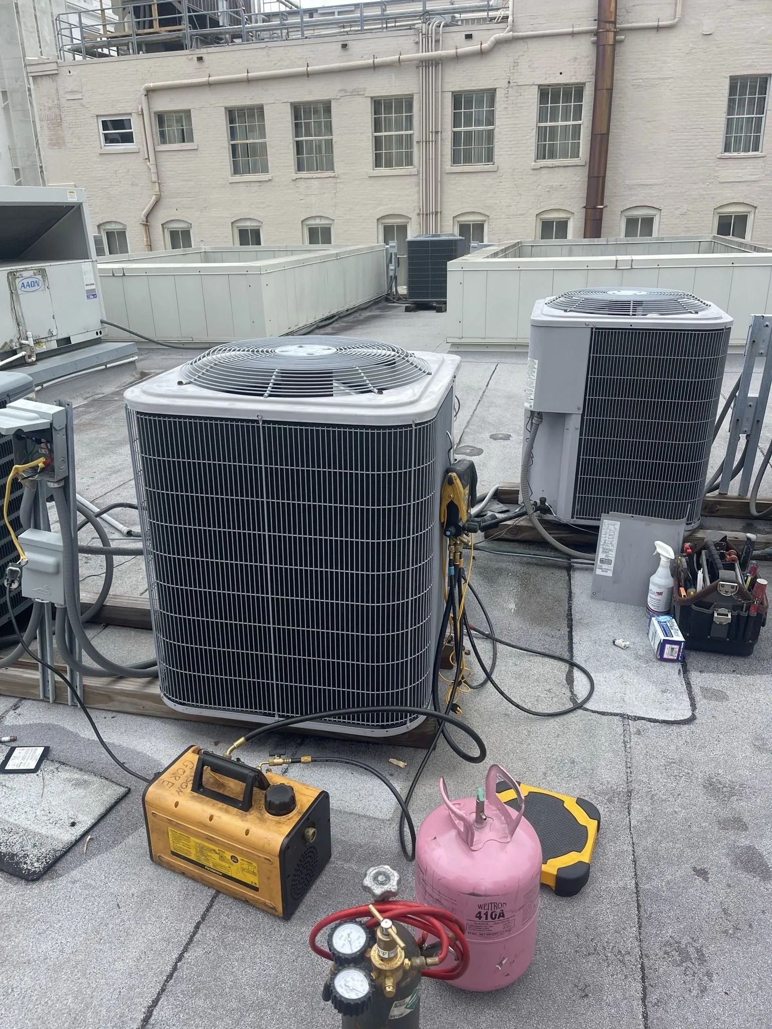 HVAC units on a rooftop being serviced. Yellow and pink tanks, tools, wiring visible.