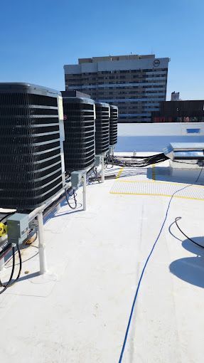 A row of air conditioners are sitting on top of a white roof.