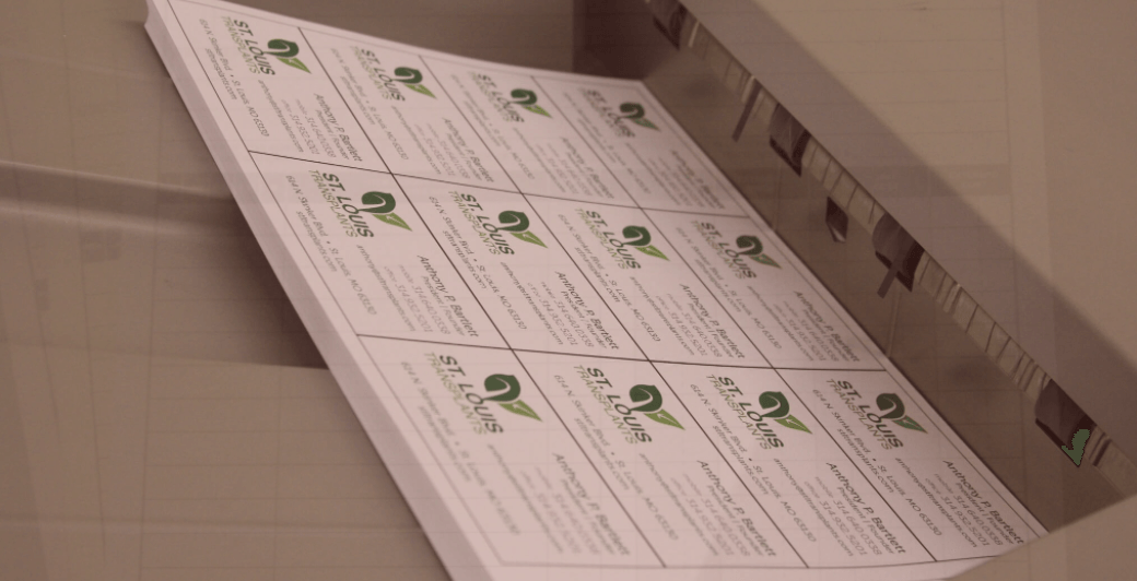 Sheets of printed business cards in a printer tray, stacked, with a green logo repeated.