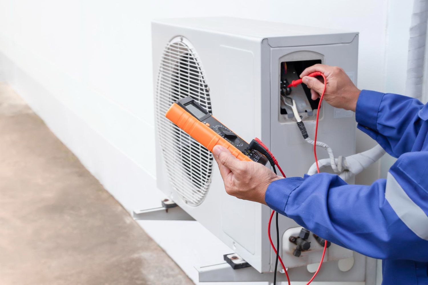 Technician testing an outdoor HVAC unit with a multimeter and orange tool case