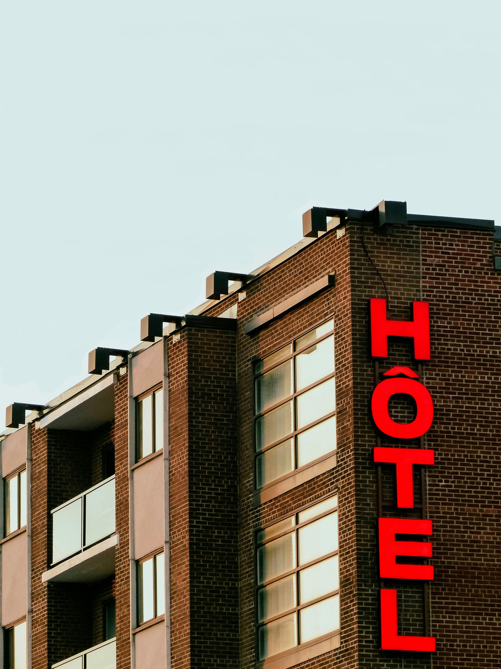 Brick hotel building with large red vertical “HOTEL” sign against a pale sky