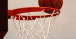 Basketball going through a red hoop with a white net