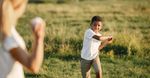 Two people outdoors in a field, one boy reaching out while another stands blurred in the foreground.