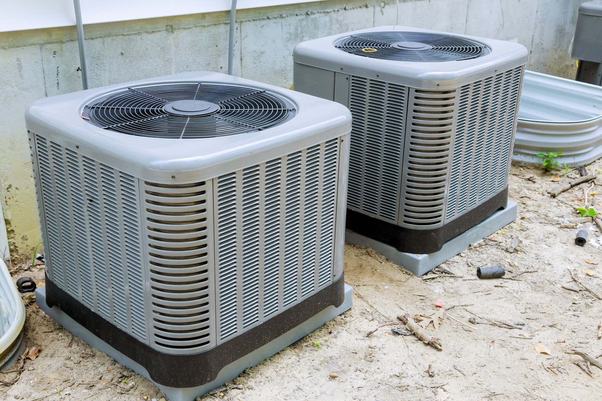 Two air conditioners are sitting on the ground next to each other.