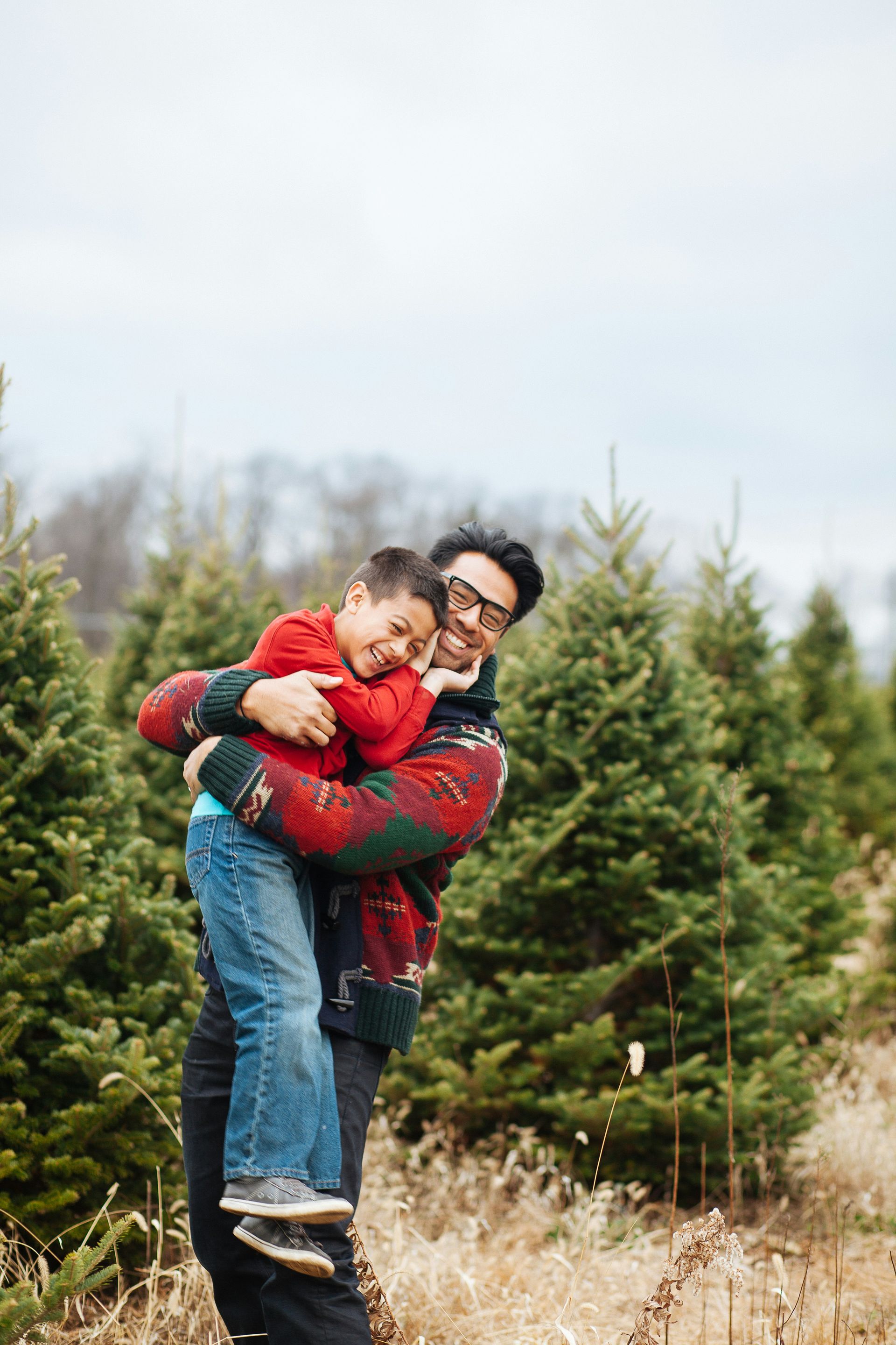 A man is holding a little boy in his arms at a christmas tree farm.