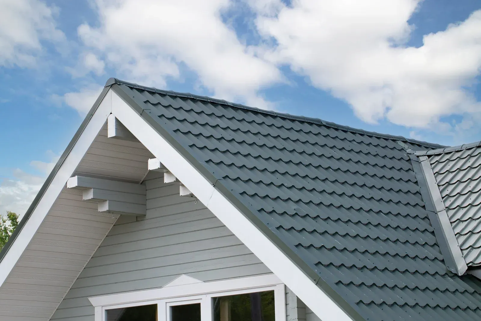 A light gray house with a gray tiled roof against a blue sky with fluffy white clouds.