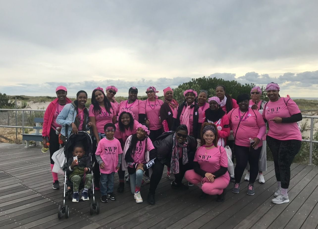 A group of people wearing pink shirts are posing for a picture on a wooden deck.