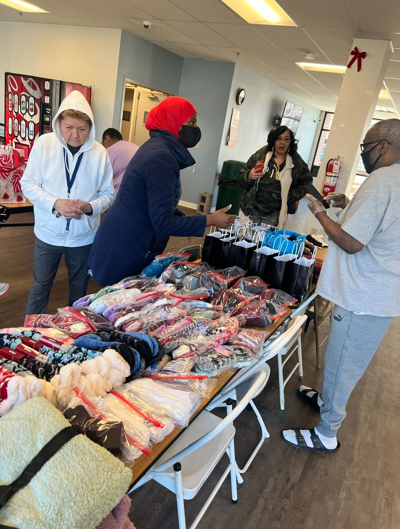 A group of people are standing around a table with a lot of items on it.