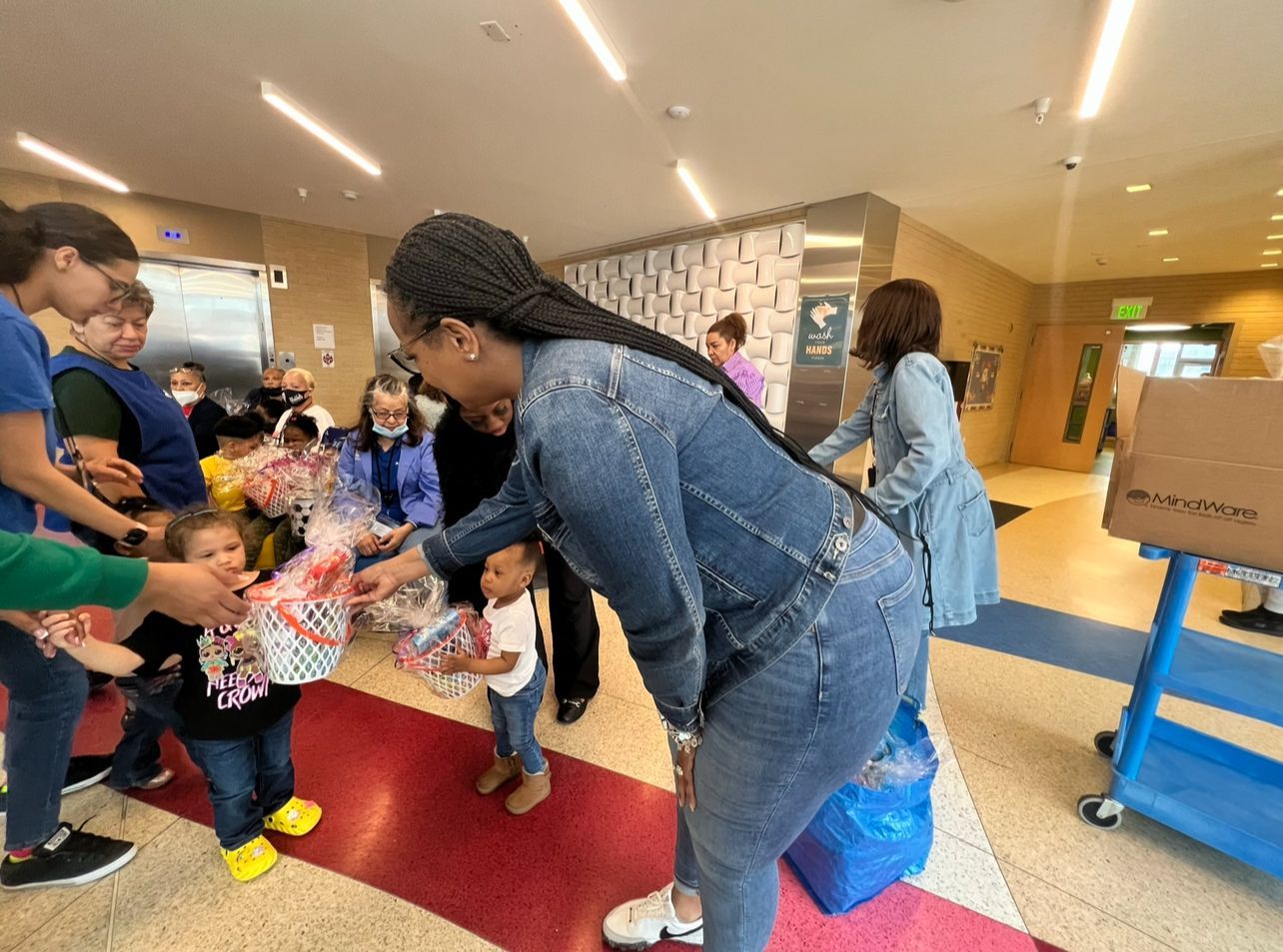 A woman is giving a gift to a child in a hallway.