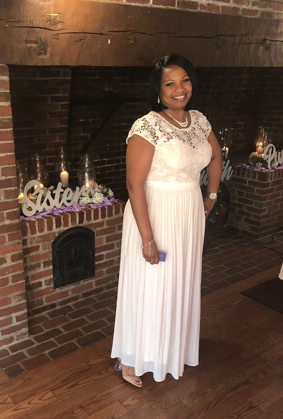 A woman in a white dress is standing in front of a fireplace.