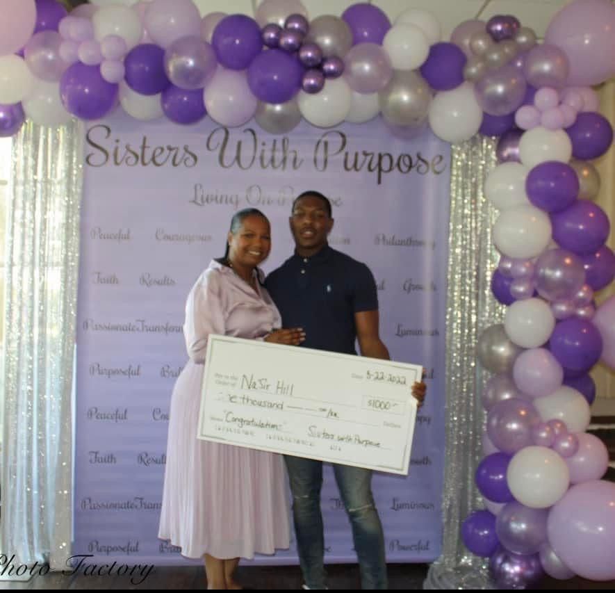 A man and woman holding a check in front of a sign that says sisters with purpose