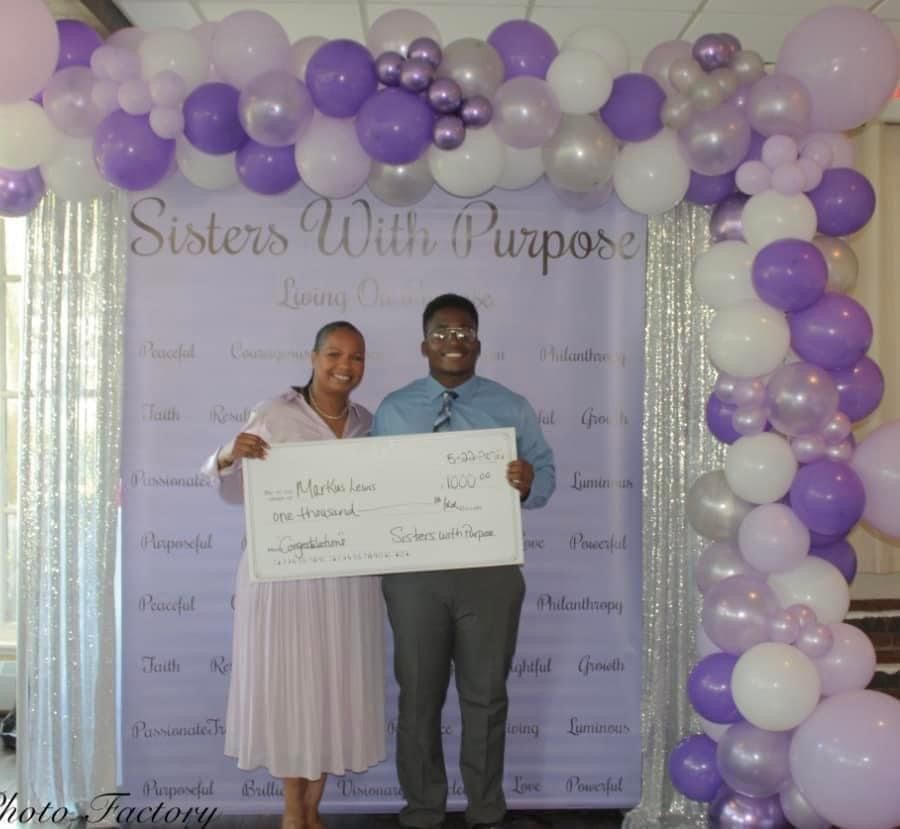 A man and woman holding a check in front of a sign that says sisters with purpose
