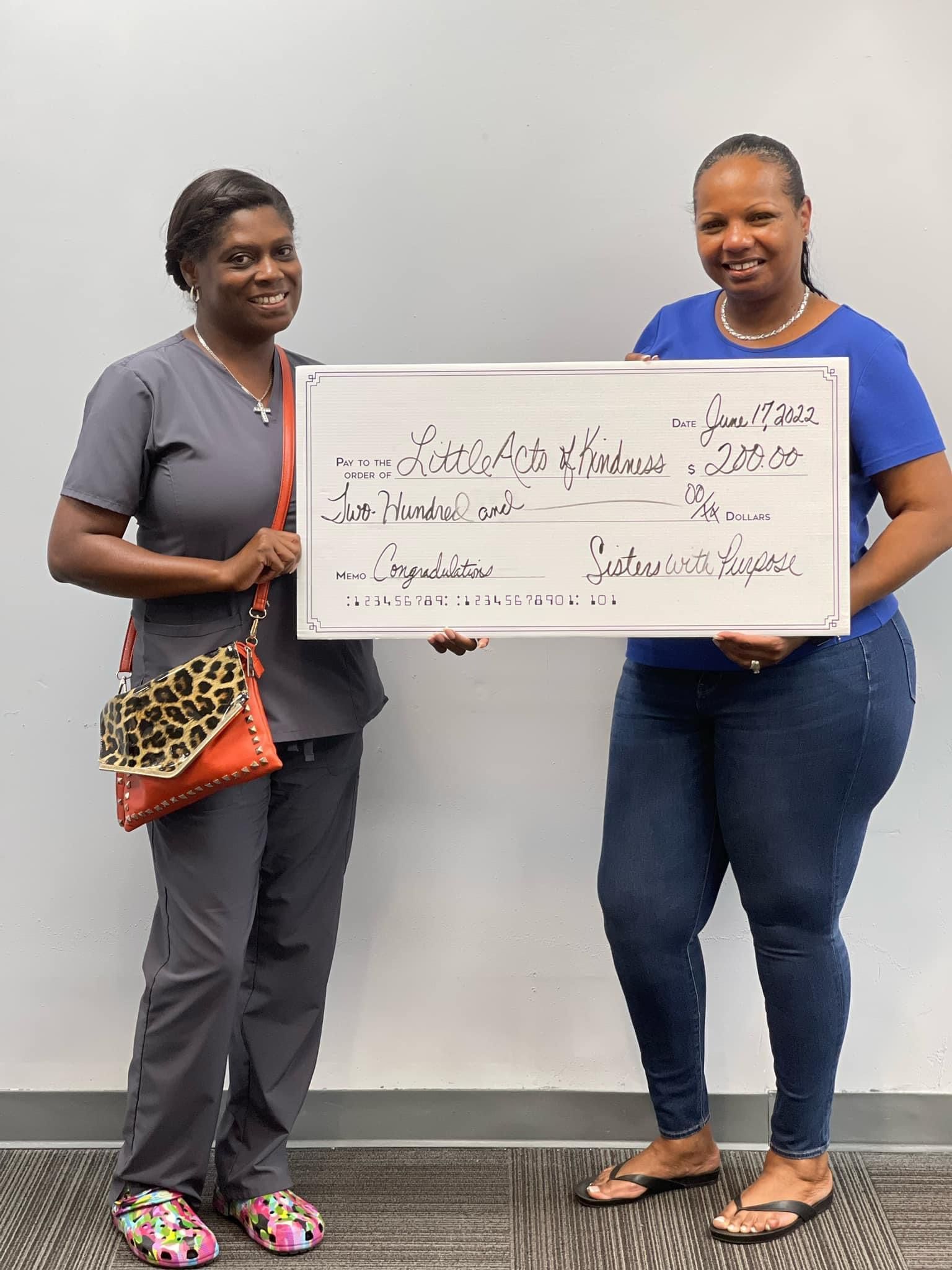 Two women are standing next to each other holding a large check.