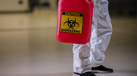 A person is holding a red container with a biohazard sign on it.