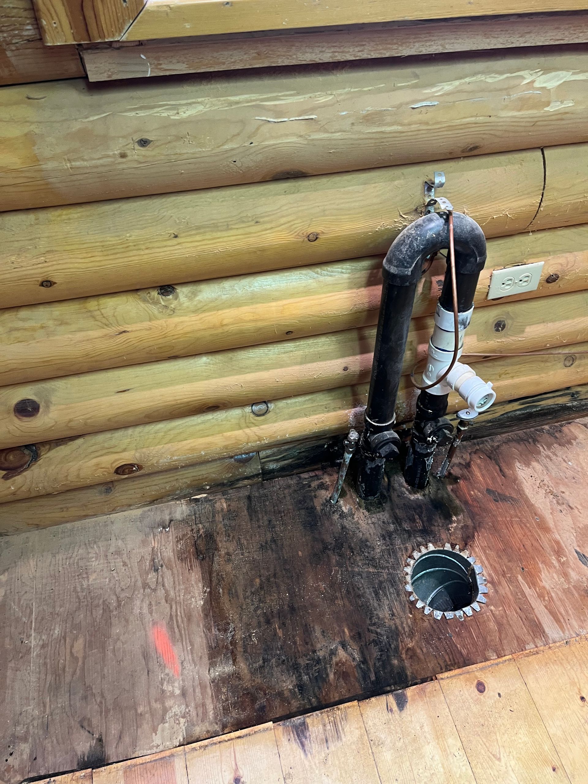 A pipe is connected to a hole in the floor of a log cabin.