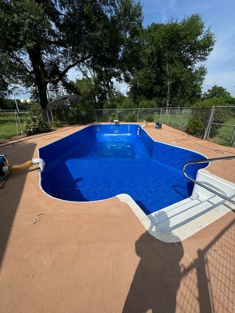 A large blue swimming pool is surrounded by trees and a fence.